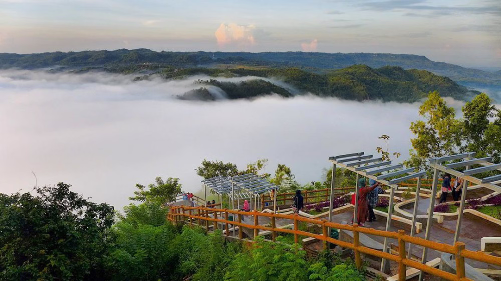 Pemandangan indah dari bukit dengan kabut menutupi lembah, pengunjung menikmati keindahan alam dan suasana tenang.