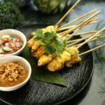 Sate ayam lezat disajikan dengan saus kacang dan sambal segar, mengundang selera dengan cita rasa otentik Indonesia.