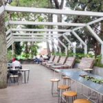 Ruang santai modern dengan desain terbuka, dikelilingi pepohonan hijau, tempat ideal untuk berkumpul dan bersantai.
