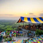 Tempat makan outdoor dengan tenda warna-warni, menawarkan pemandangan indah matahari terbenam dan area santai di atas bukit.
