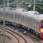 Kereta listrik melintasi tikungan rel di perkotaan, menunjukkan transportasi umum yang efisien dan modern di Indonesia.