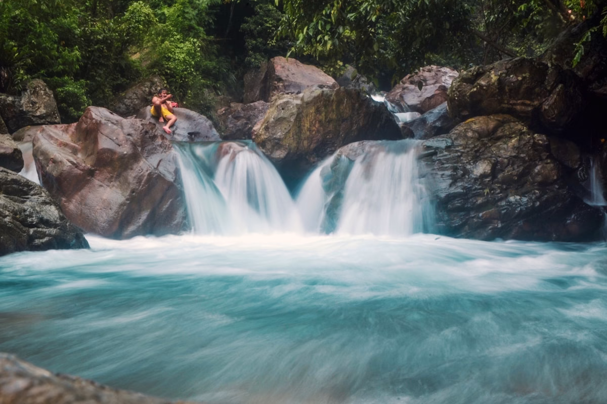 Pasangan bahagia menikmati waktu bersama di tepi air terjun yang menenangkan dikelilingi oleh hutan lebat.
