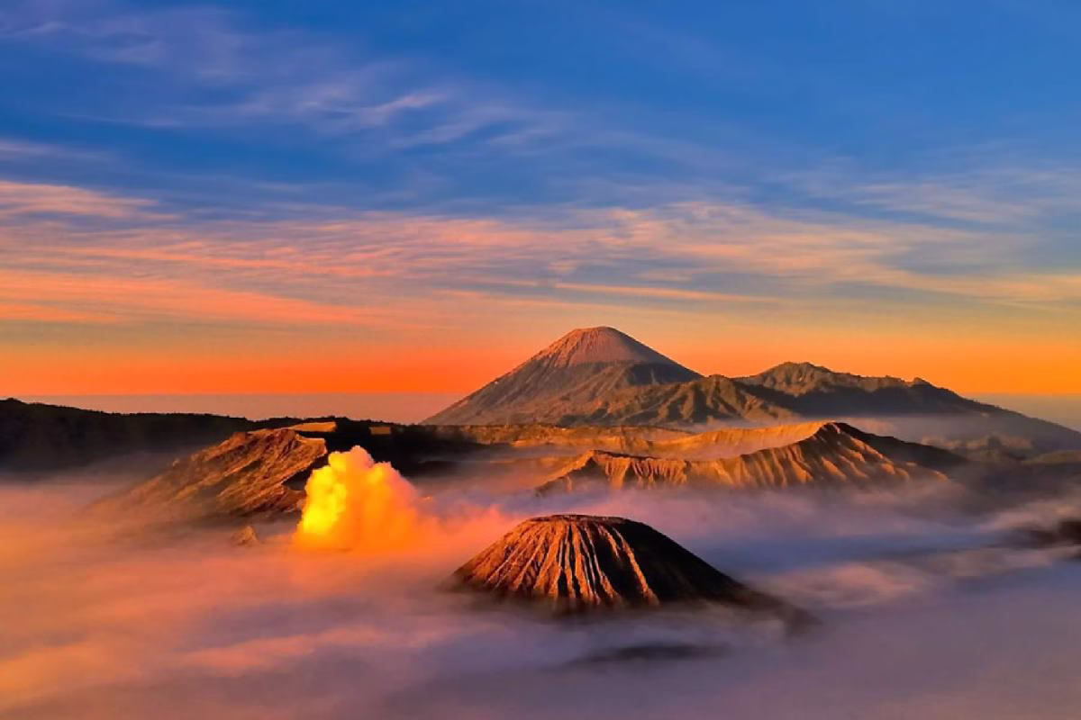 Breathtaking sunrise over Bali’s volcanic landscape, featuring Mount Bromo's steam amidst dramatic clouds and mountains.