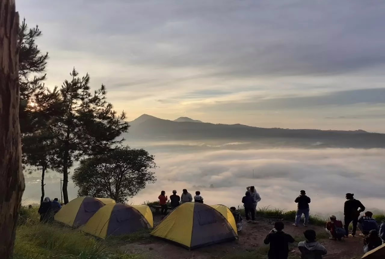 Pemandangan indah para pendaki menikmati matahari terbit di atas lautan kabut, dikelilingi tenda kemah di pegunungan.