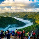 Pemandangan indah dari puncak dengan pengunjung menikmati kabut pagi di lembah hijau yang subur.