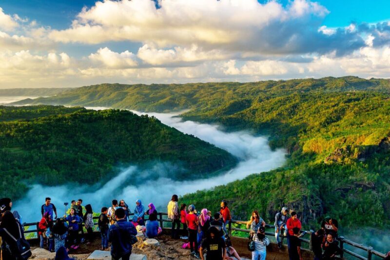 Pemandangan indah dari puncak dengan pengunjung menikmati kabut pagi di lembah hijau yang subur.