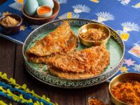 "Piring hidangan rendang tradisional dengan keripik dan telur setengah matang, dikelilingi oleh rempah-rempah berwarna cerah."