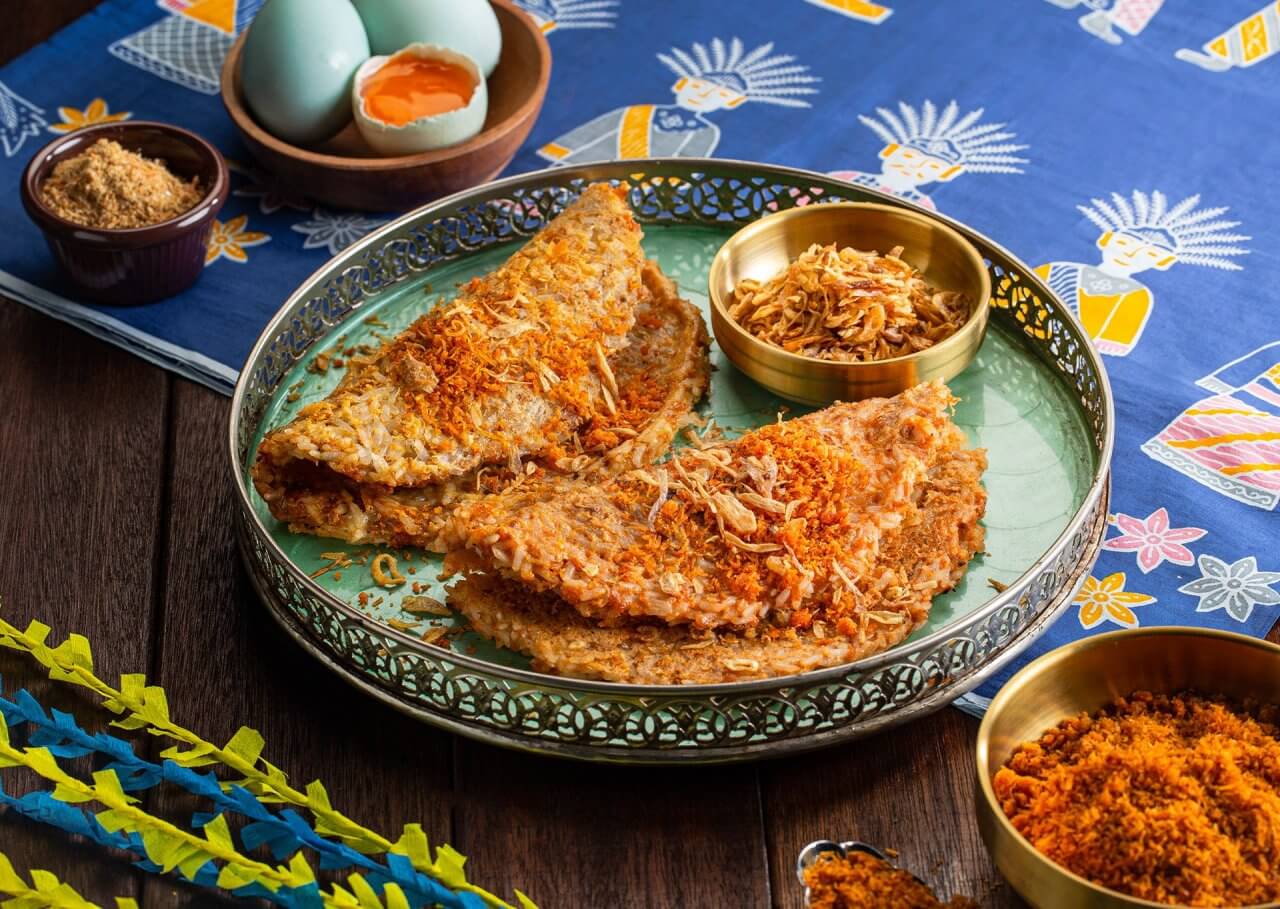 "Piring hidangan rendang tradisional dengan keripik dan telur setengah matang, dikelilingi oleh rempah-rempah berwarna cerah."