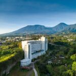 Hotel modern yang dikelilingi pemandangan pegunungan dan kebun hijau, menciptakan suasana alami yang menenangkan.