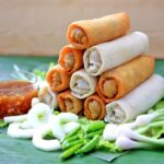 Lumpia goreng renyah disajikan dengan saus sambal dan sayuran segar, menciptakan hidangan yang menggugah selera.