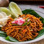 Mie Aceh pedas khas Indonesia disajikan dengan irisan mentimun, sambal, dan kerupuk, menciptakan hidangan menggugah selera.