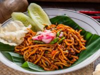 Mie Aceh pedas khas Indonesia disajikan dengan irisan mentimun, sambal, dan kerupuk, menciptakan hidangan menggugah selera.