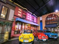 Kota miniatur dengan mobil klasik warna-warni di depan restoran Prancis yang memukau dan suasana yang penuh pesona.
