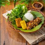 Porsi nasi dengan lauk tradisional, sayuran segar, dan sambal, menggambarkan kelezatan masakan Indonesia yang autentik.