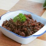 Sambal teri pedas dengan bumbu kaya rasa, disajikan dalam mangkuk putih dengan hiasan peterseli segar.