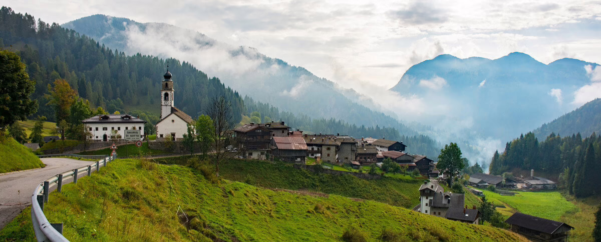 Pemandangan Desa Wisata Sauris-Zahre Italia pegunungan yang tenang dengan awan berkabut, dikelilingi hutan dan gunung yang indah.